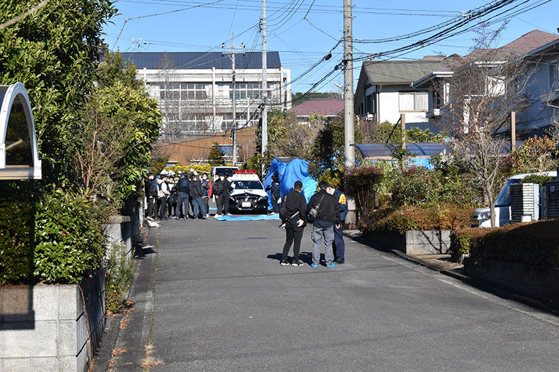 男女3人が殺害された住宅周辺を捜査する警官ら。現場は閑静な住宅街で、近隣には中学校（写真奥）もある＝25日午前9時42分、埼玉県飯能市美杉台