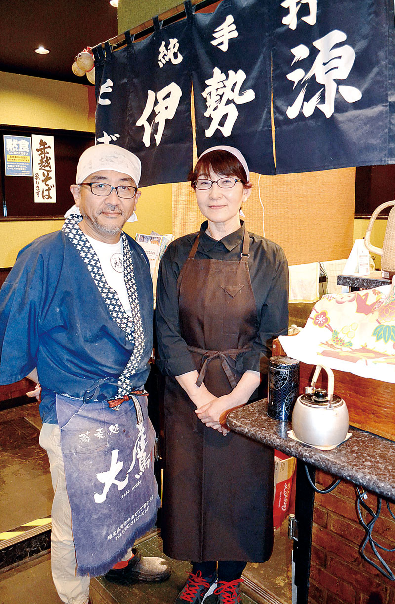 二人三脚で店を切り盛りする池田真介さんと妻の志津さん。カウンターには池田さんが弟子入りした老舗蕎麦店「伊勢源」から譲り受けたのれんをオブジェとして飾っている