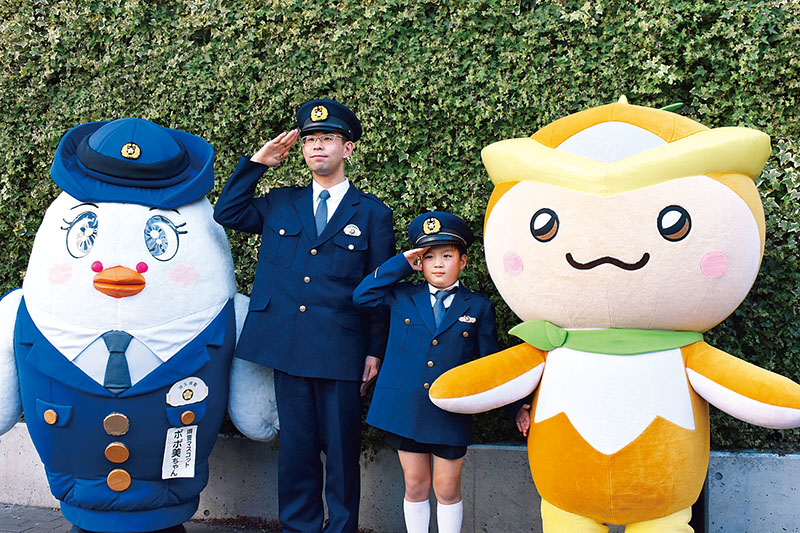 敬礼する加藤虎士さん（中央右）と熊井明弘さん＝9日午前、所沢市日吉町の西武線所沢駅西口