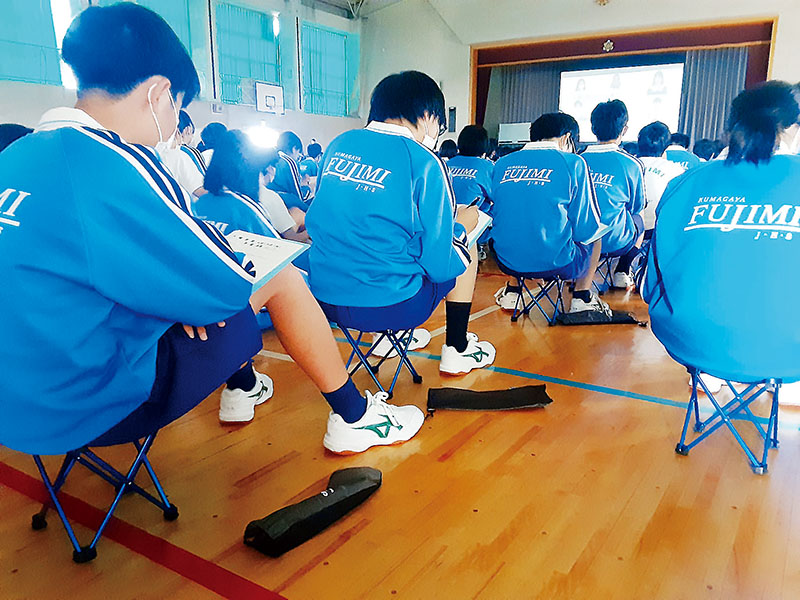 全校集会で体育座りに替わって携帯型パイプ椅子に座る男子生徒たち＝熊谷市立富士見中学校