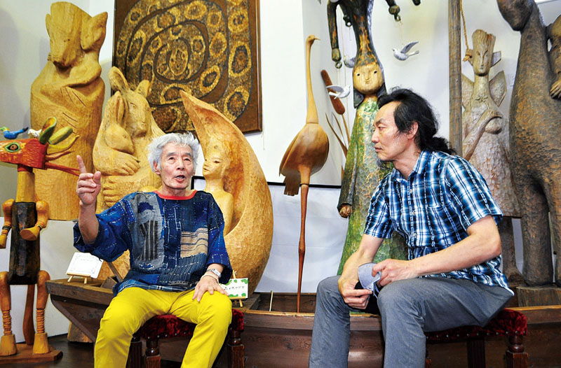 「モッキンカン木の森美術館」で彫刻家しまずよしのりさん（左）に話を聞く近藤良平さん。住宅街の中にある美術館にもかかわらず、数メートルを超える大型作品が並ぶ＝6月16日、さいたま市内