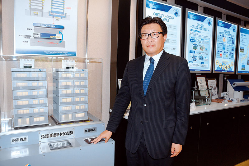 建築物の免震構造に施した樹脂コーティングを紹介する模型など、業務の説明が並ぶエントランスに立つ諏訪部充弘社長＝埼玉県川越市芳野台