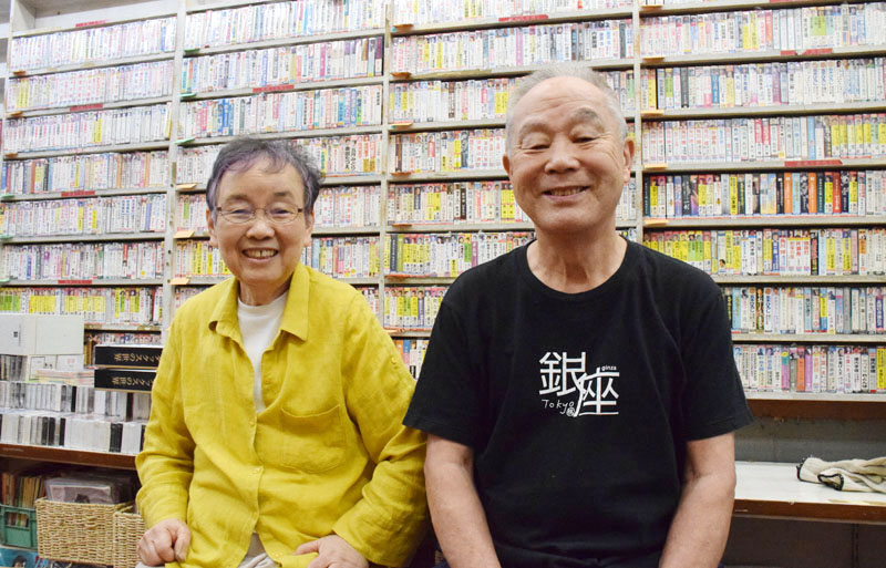 棚にびっしりと並ぶ演歌のカセットテープを前に、「あっという間の55年だった」と語る松下良夫さん（右）と佳代子さん＝蕨駅前の「ミヤコ」