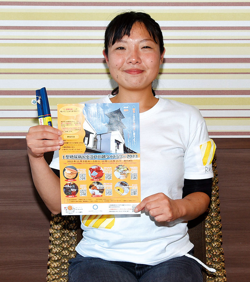 自身がデザインしたインスリン自己注射をしやすいTシャツを着用し、注射器やチラシを手にクイズラリーへの参加を呼びかける吉田恵さん