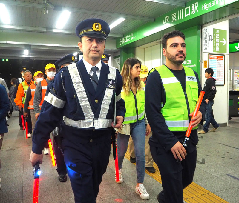 JR東川口駅付近をパトロールする警察官と日本クルド文化協会のワッカス・チカン代表理事（右）＝4日午後5時45分ごろ