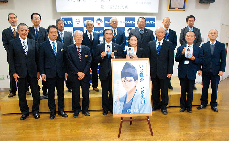偉人マンガ発行記念式典で「いざ鎌倉　いざ嵐山―」を手にする佐久間孝光町長（前列左から4人目）ら＝埼玉県嵐山町役場町民ホール