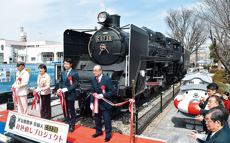 再塗装された蒸気機関車（SL）のC5726号の前で、テープカットを行った行田邦子市長（左から2人目）ら＝24日午前、埼玉県行田市本丸の本丸児童公園蒸気機関車展示場