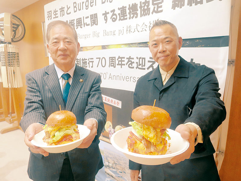 連携協定締結後、ハンバーガーを持つ渡辺貴広さん（右）河田晃明市長＝羽生市役所