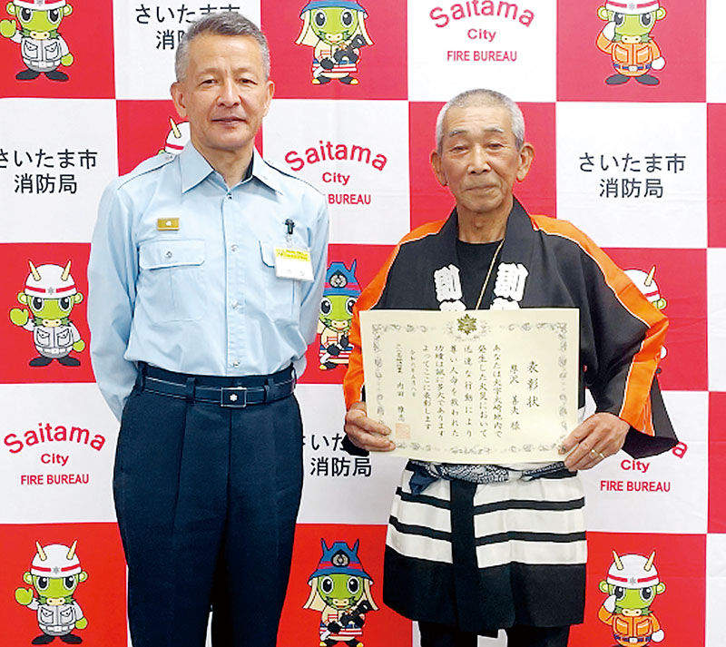 内田雅志緑消防署長（左）から表彰状を受け取った厚沢善夫さん＝8日、埼玉県さいたま市緑区の緑消防署