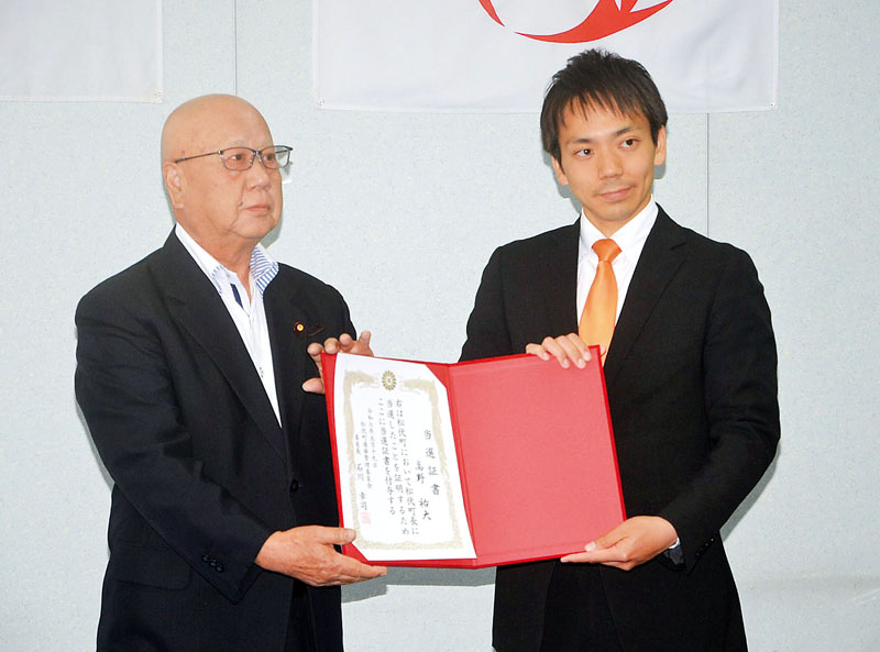 当選証書を手に写真撮影に応じる高野祐大氏＝19日午後2時過ぎ、松伏町役場