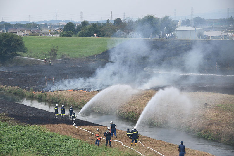 燃え広がる河川敷の火災と消火活動を行う消防隊員
