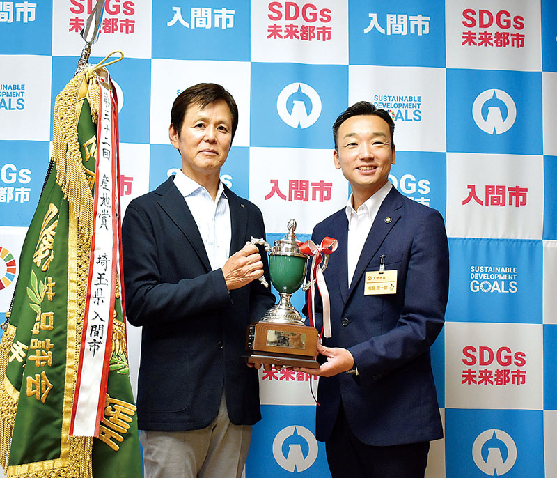 一等一席を受賞した間野隆司さん（左）＝8月22日午前、入間市役所