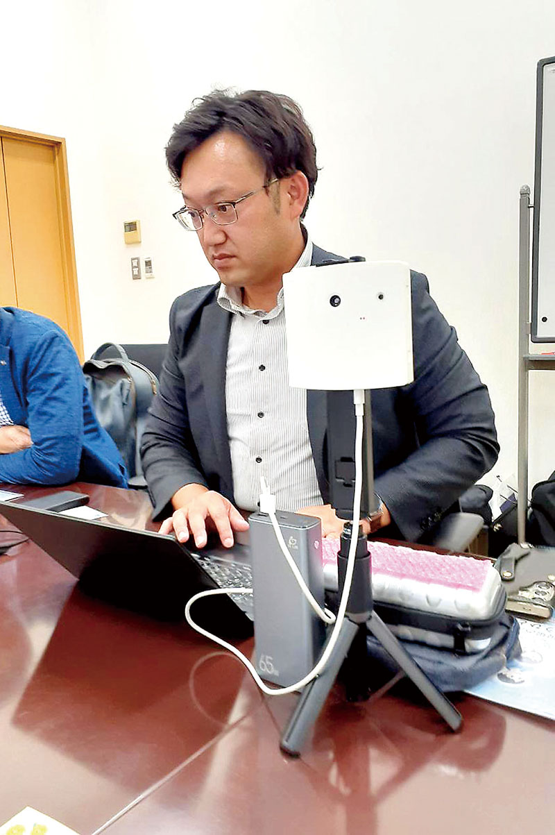 「フィンガルリンクコネクト」（手前の機器）とパソコン上で介護者の状態を確認する担当者