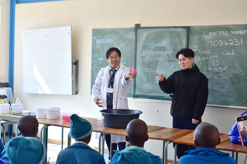 南アの小学生の前で大気圧の実験を披露する石塚祐貴さん（左）と古屋雅大さん