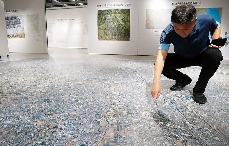 さいたま市内全域を3千分の1に縮小した空中写真。地図展推進協議会事務局の大滝修さんが示しているのは大宮公園周辺＝26日、さいたま市大宮区のレイボックホール