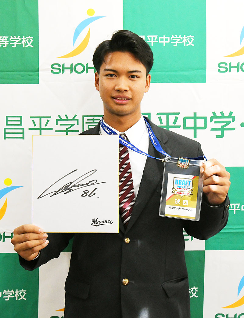 指名あいさつ後、ロッテのサブロー新監督のサイン色紙とドラフト会議の球団パスを掲げる昌平高の桜井ユウヤ内野手＝29日午後、杉戸町の同校