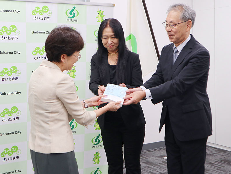 完成した本をさいたま市の竹居秀子教育長（左）に手渡す桐田寿子さんと桐淵博さん＝14日、さいたま市浦和区のさいたま市役所