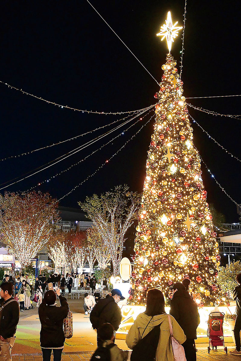 点灯して輝く巨大なクリスマスツリーを眺める来場者たち。奥はけやきウォークのイルミネーション