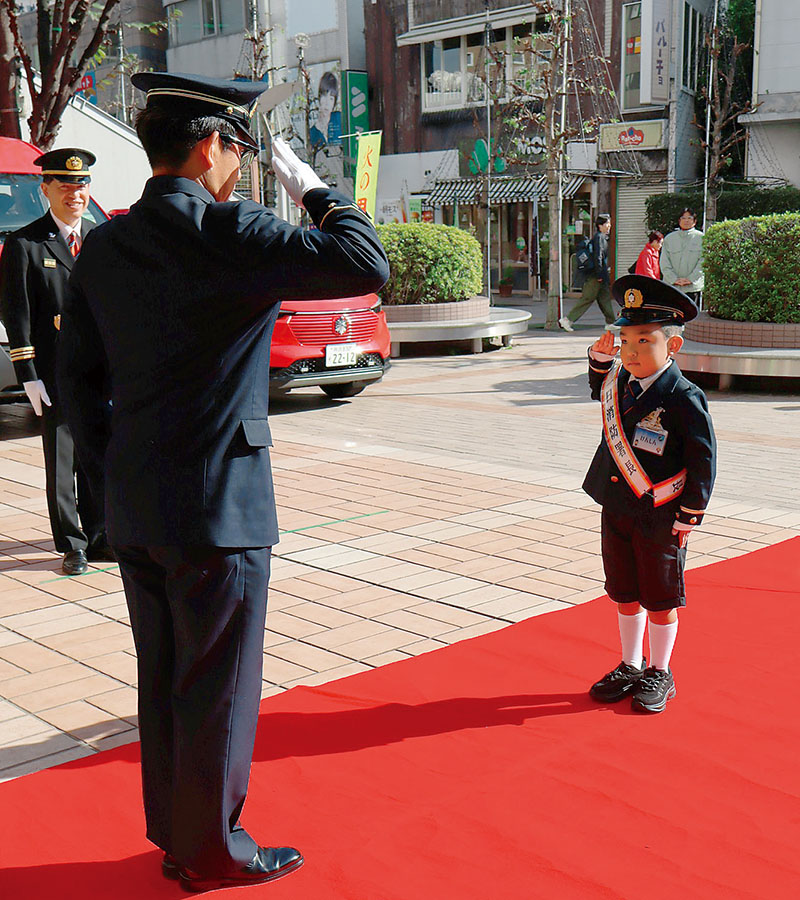 志木消防署の関口敬行署長（左）から1日署長の委嘱状授与を受け、敬礼する綱島健心さん＝東上線志木駅東口駅前広場