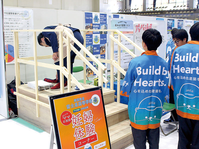 県立富士見高校「ぼくたちママ応援隊」の高校生に見守られながら妊婦体験をする参加者ら＝11月8日午後、上尾市民体育館