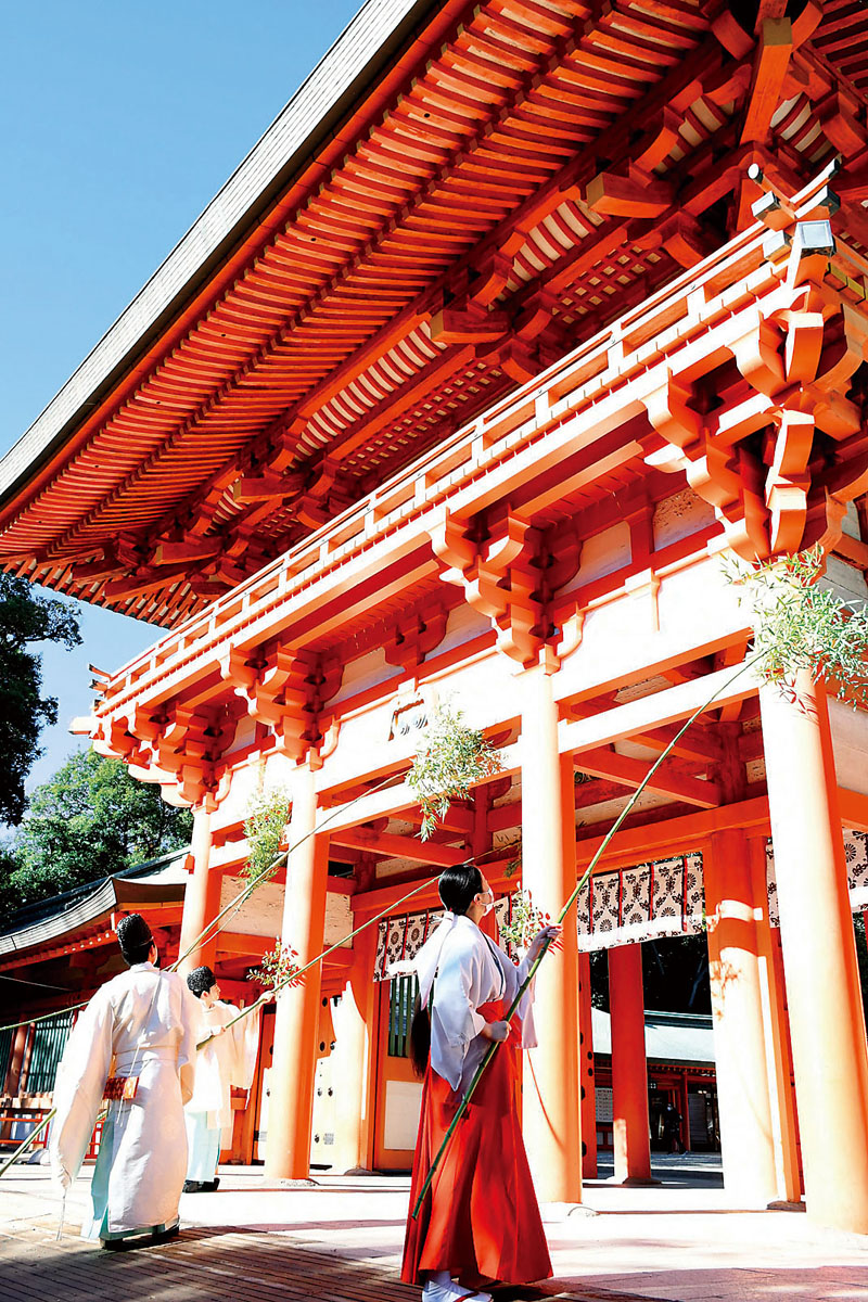 葉の付いた長い竹を使い、楼門を清める神職、巫女たち＝15日午前、さいたま市大宮区の氷川神社