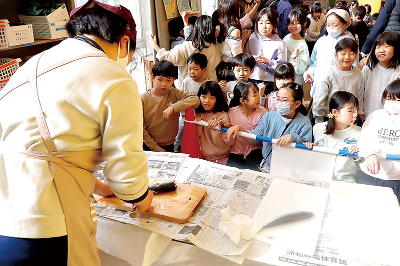 児童らの前でアジの三枚おろしを実演する和光市第二中学校区地域学校協働本部の女性＝和光市立本町小学校