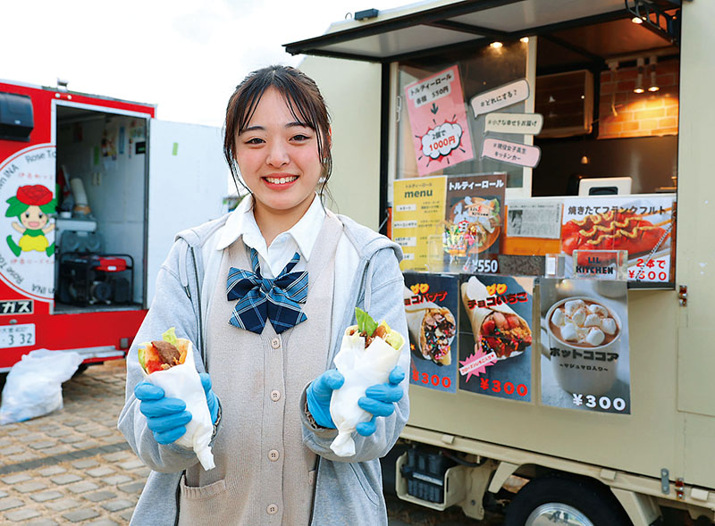 大人気の「ミートトルティーロール」を笑顔で差し出す八木杏妃さん