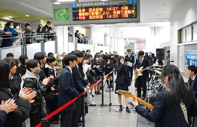 閉鎖する改札内で演奏する生徒と手拍子する観客ら＝11日午後、本川越駅