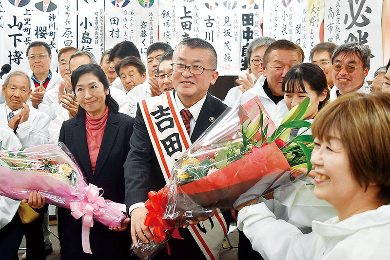 無投票で6選を決め、笑顔で花束を受け取る吉田信解氏（中央）＝18日午後5時半、本庄市東台の事務所