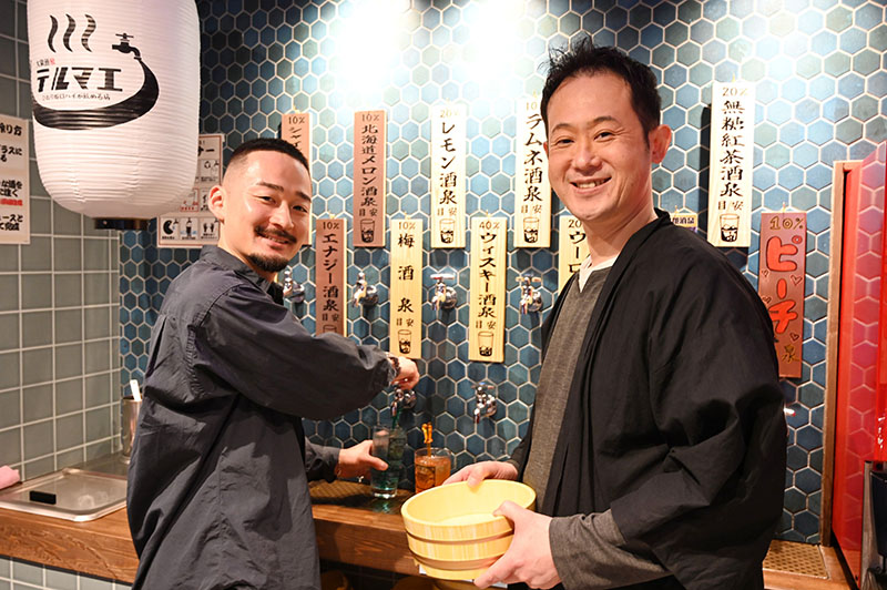 「水道の蛇口からお酒を注ぐ非日常感を楽しんで」と話す高橋光基社長（左）とFC店オーナーの渡辺靖之代表＝川越市の大衆酒泉テルマエ本川越駅クレアモール泉