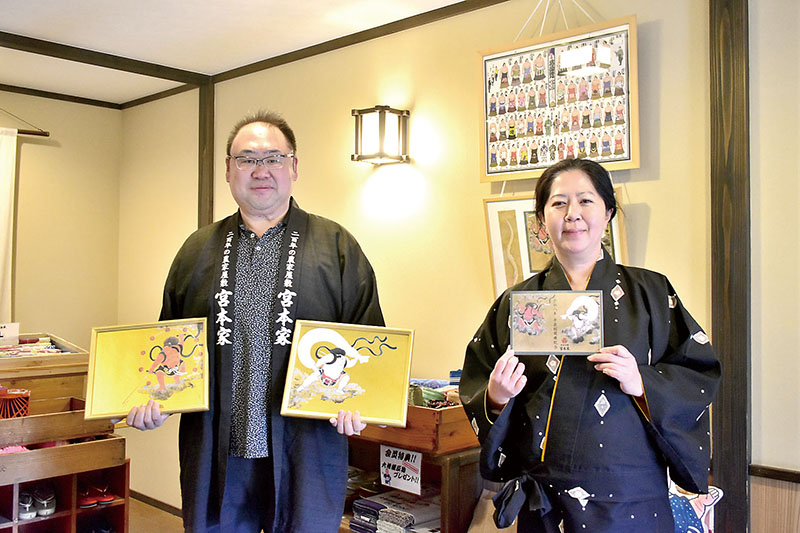 木下大門さんが描いた風神雷神図と限定御朱印を紹介する、宮本一輝さん（左）と女将の愛さん