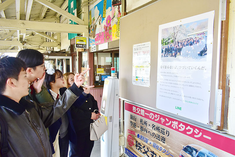 卒業を祝うサプライズのポスターに歓喜する皆野高校3年生と保護者＝7日午前8時半ごろ、秩父鉄道皆野駅