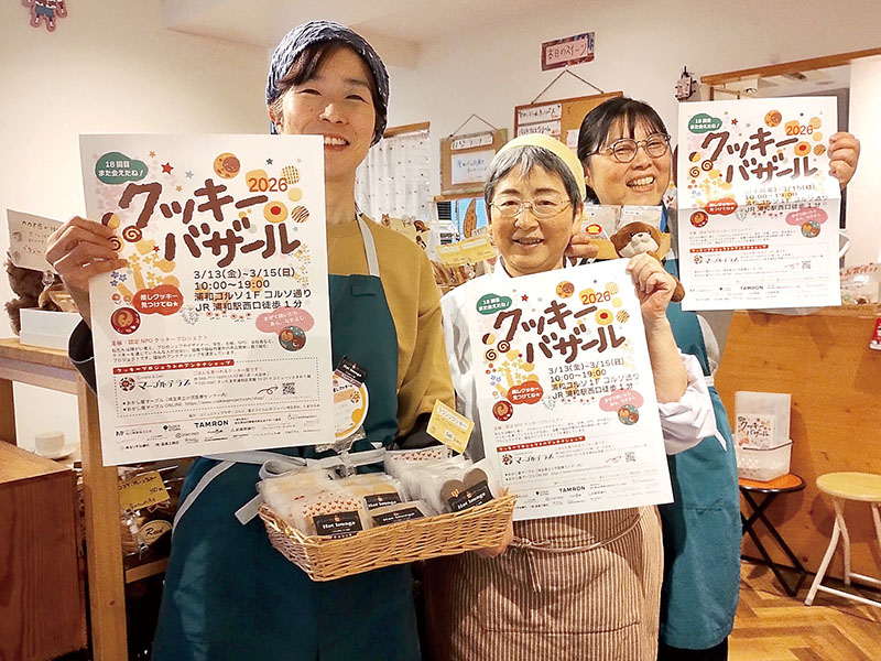 スタッフと一緒にクッキーバザールのチラシと自身の“推しクッキー”を持つ若尾明子さん（左）