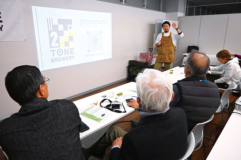 アンズのクラフトビールを試飲しながら代表の福岡浩司さんの説明を聞く参加者＝鳩山町松ケ丘の鳩山コミュニティ・マルシェ