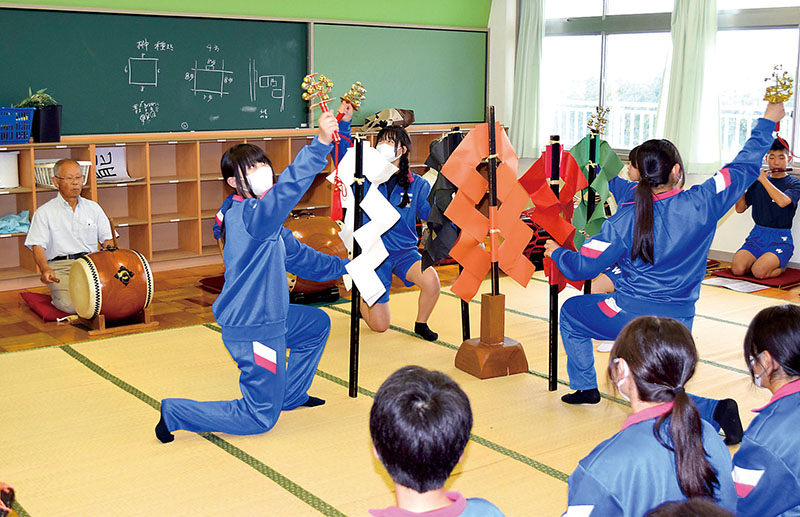 3年生の引退公演に向け、神楽の稽古に励む郷土芸能部の部員と、指導する初代顧問の川井一弘さん（左）＝10日午後、久喜市立鷲宮中学校