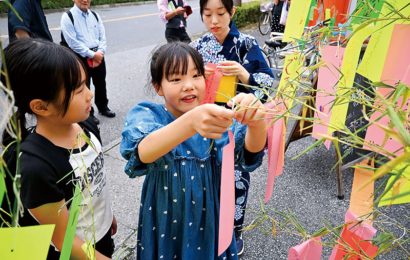 短冊を笹にくくり付ける小学生たち＝3日午後、越谷市千間台西の七夕祭りイベントスペース