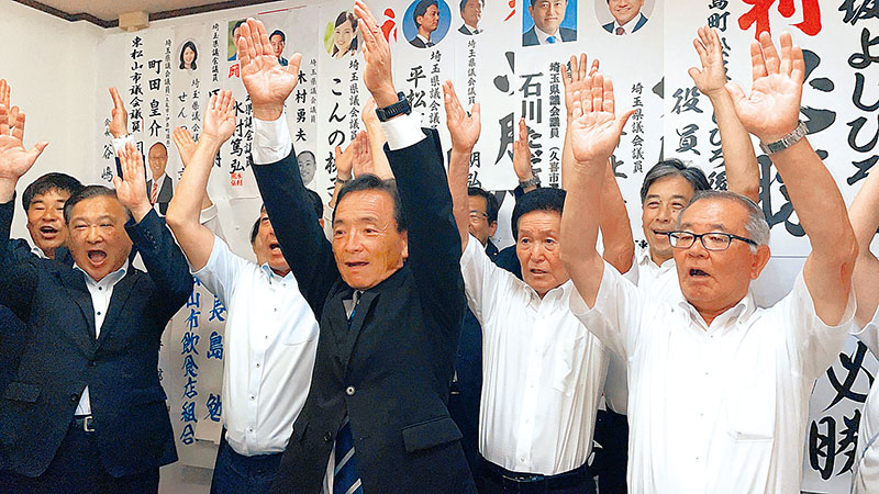 支持者と万歳をして当選を喜ぶ松坂喜浩氏（中央）＝12日夜、東松山市材木町の選挙事務所