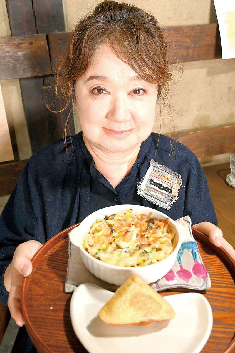 「ピなり」（手前）を手にする名付け親のはかまだみさこさん。奥の料理が「ナピラ」＝本庄市千代田の「NINOKURA」