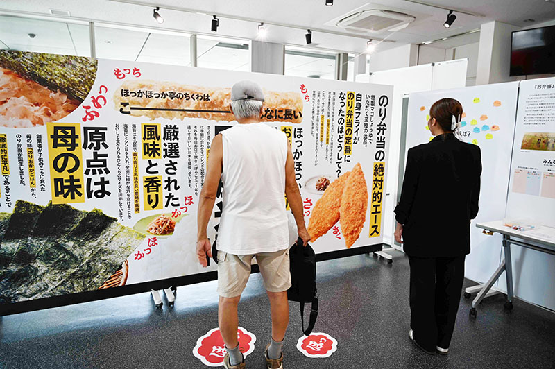 巨大パネルの説明文を読む来場者ら