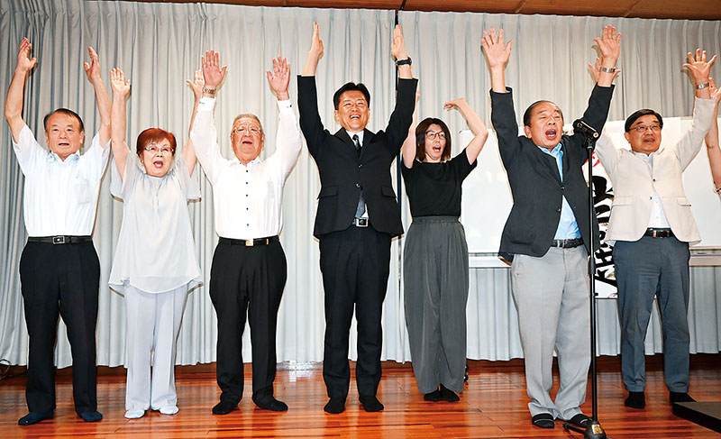 支持者らと万歳をして、再選の喜びを分かち合う峯岸克明氏（中央）＝9日午後10時10分ごろ、寄居町保田原の選挙事務所