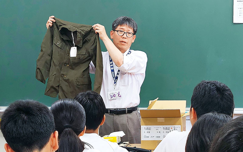 実際に使われていた国民服を手に熱く語る大井さん＝熊谷市立富士見中学校