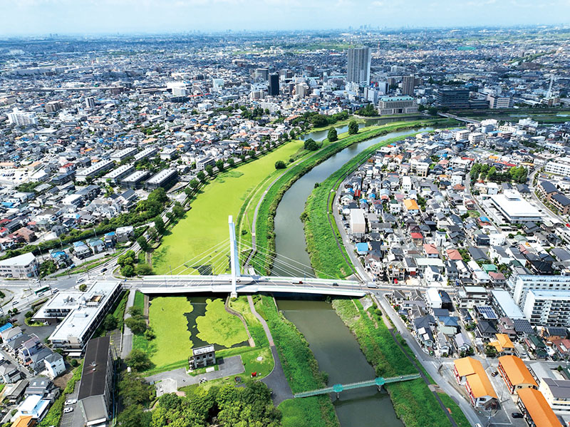 越谷市の葛西用水瓦曽根溜井周辺。越谷市役所近く上空をドローンにより撮影。右上が越谷市役所、右側を流れる川が元荒川、平行して左側に葛西用水が溜井に流れ込み、水面にサンショウモが発生している＝19日、越谷市の国内測量設計株式会社加藤祐輔さん撮影、提供