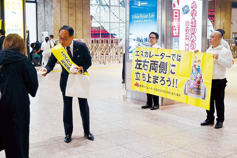 エスカレーターの安全利用キャンペーンで啓発品を配布する大野元裕知事（左）＝28日午前8時10分ごろ、さいたま市大宮区のJR大宮駅西口イベントスペース