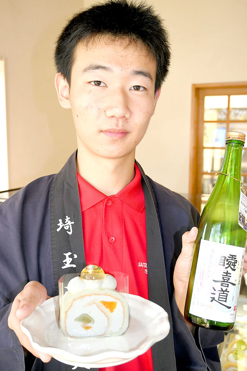 日本酒の「瞬喜道」とロールケーキを手にする西山翔太さん＝深谷市岡のロールケーキの店「そらのおかし」