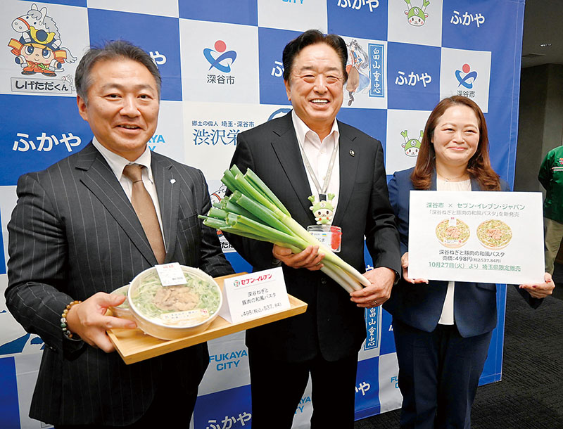 深谷ねぎを手にする小島進市長と、商品を紹介するセブン-イレブン・ジャパンの社員ら＝23日、深谷市役所