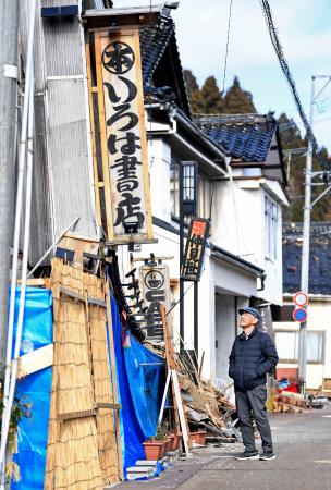 能登半島地震で全壊した「いろは書店」の前に立つ代表の八木久さん＝１７日、石川県珠洲市
