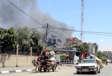 ７日、イスラエル軍による空爆で煙が上がる中、パレスチナ自治区ガザの最南部ラファから避難する人々（ゲッティ＝共同）