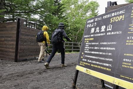 ２０２４年６月、富士山の山開きを前に山梨県側から登山に向かう人たちヘ「弾丸登山」の注意を呼びかける看板