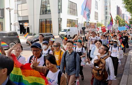 虹色の旗を掲げて札幌市中心部をパレードする参加者ら＝１４日午後