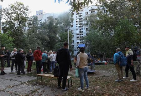 　２０日、ウクライナ東部ドニプロで、ロシアの攻撃で損壊した建物の前に立つ住人たち（ロイター＝共同）